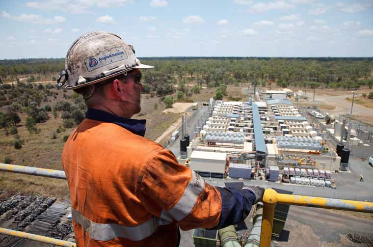 Worker in safety gear overlooking a large industrial facility under construction.