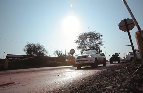 White utility vehicles driving on a sunlit road in a rural area.